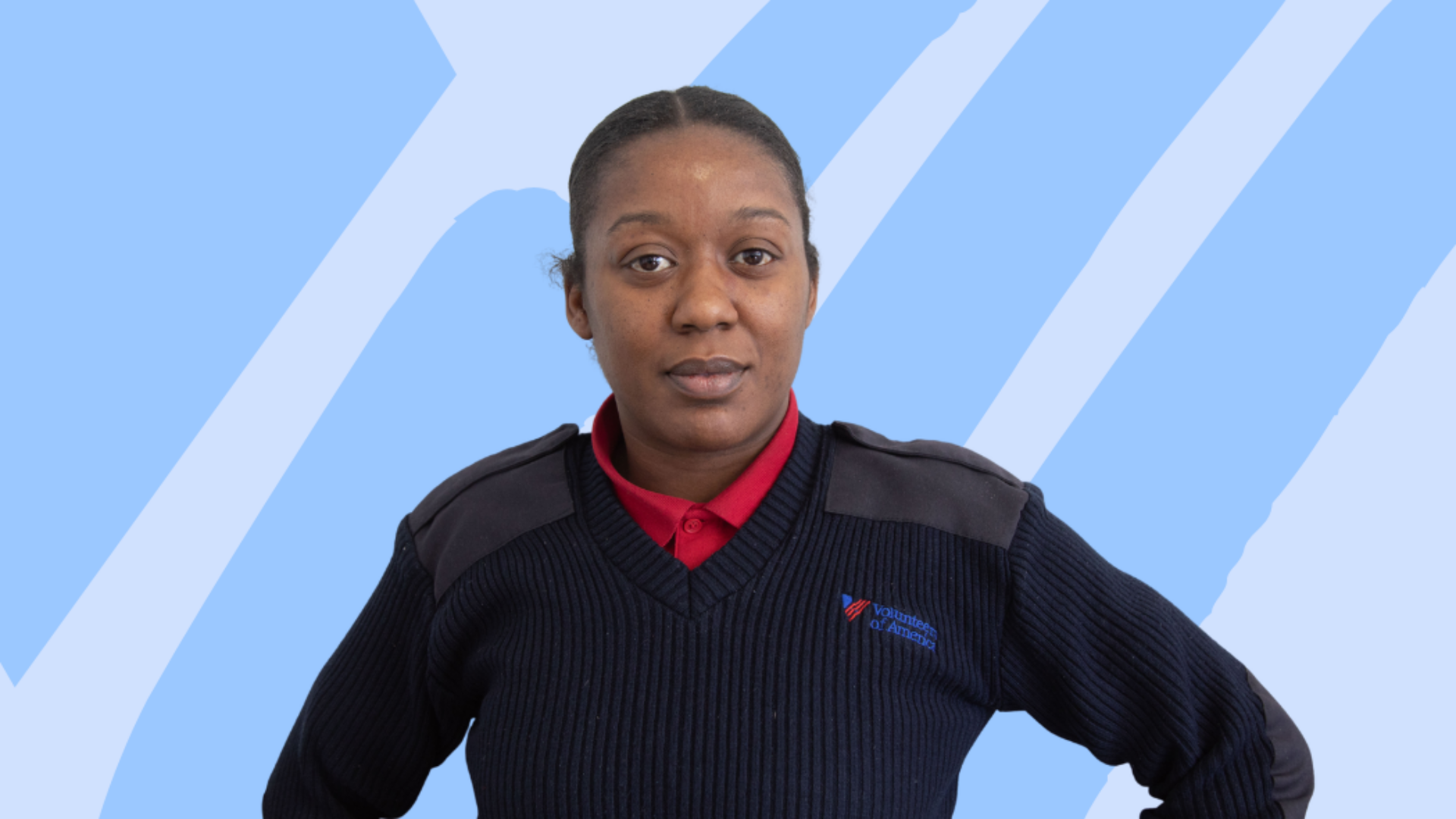 A portrait of a black woman wearing a black sweater over a red polo against a light blue background.