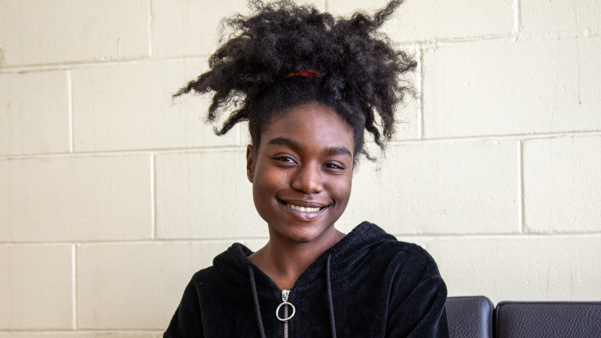 Young black woman with curly hair smiling against a white background.