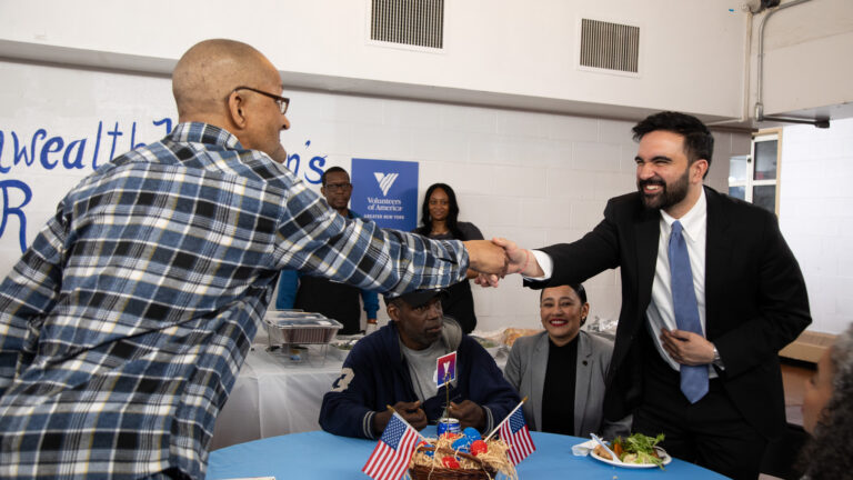 New York City Mayor Zohran Mamdani shakes hand of resident over a table.
