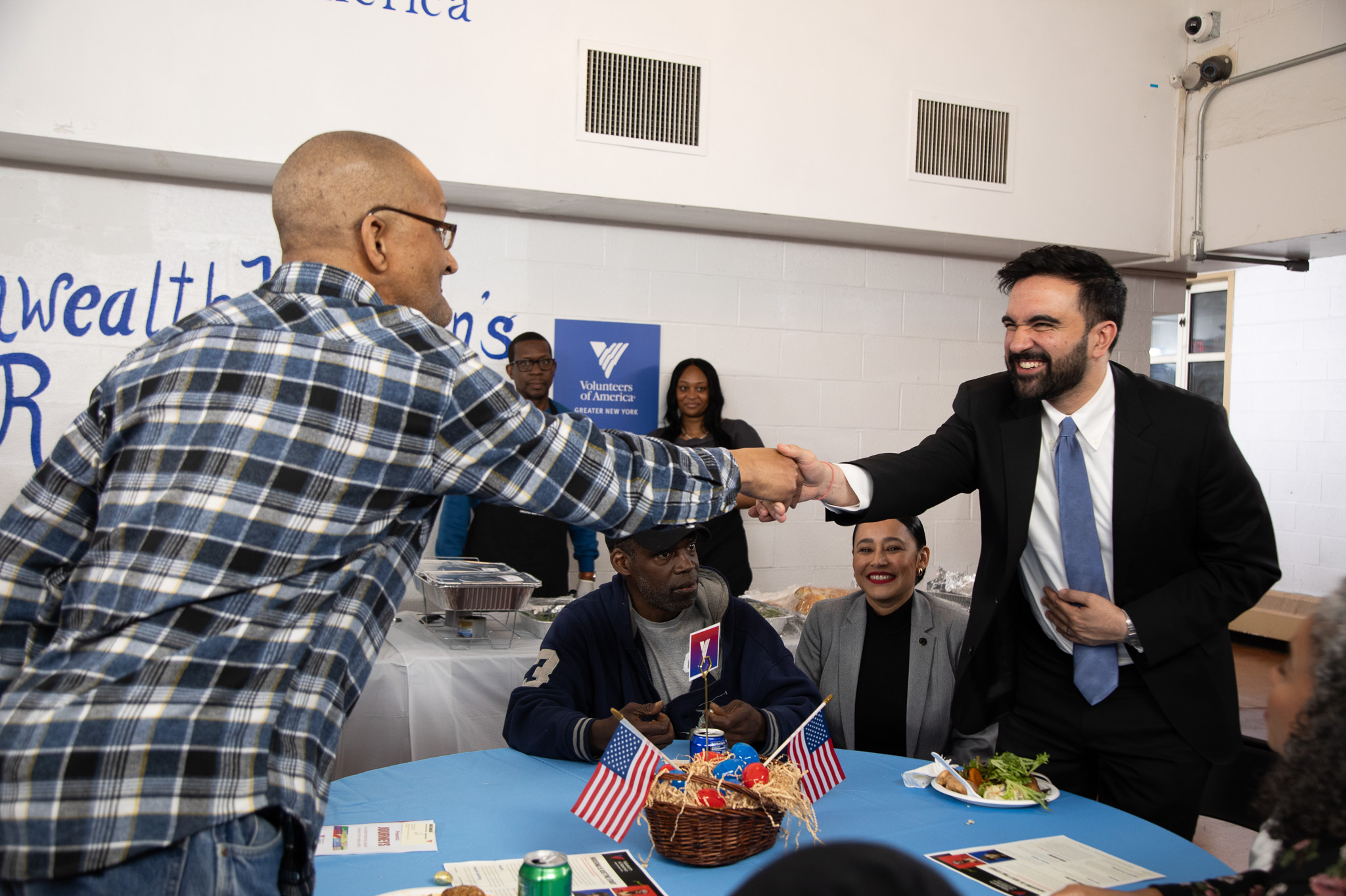 New York City Mayor Zohran Mamdani shakes hand of resident over a table.