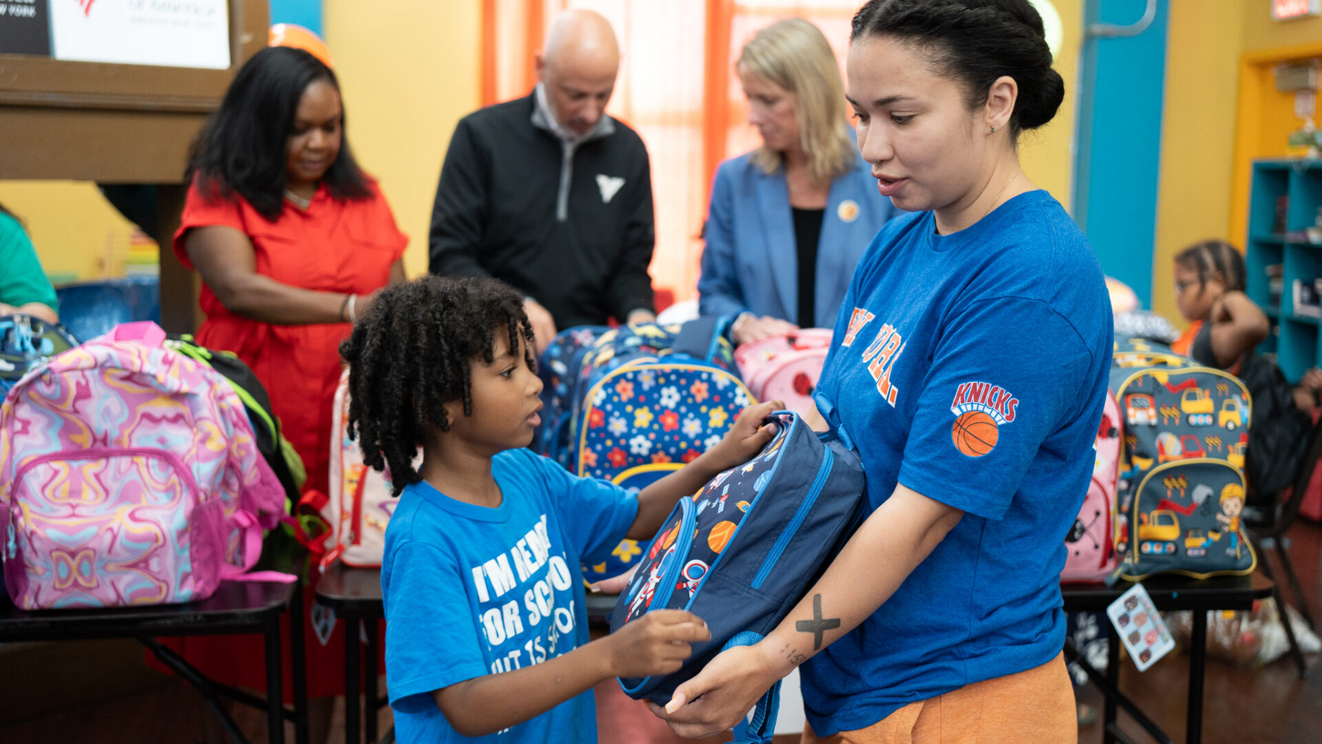 A mother holding a backpack to her child while he unzips it.