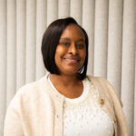 Leslie Armstrong smiles for the camera, wearing a white top and beige sweater.