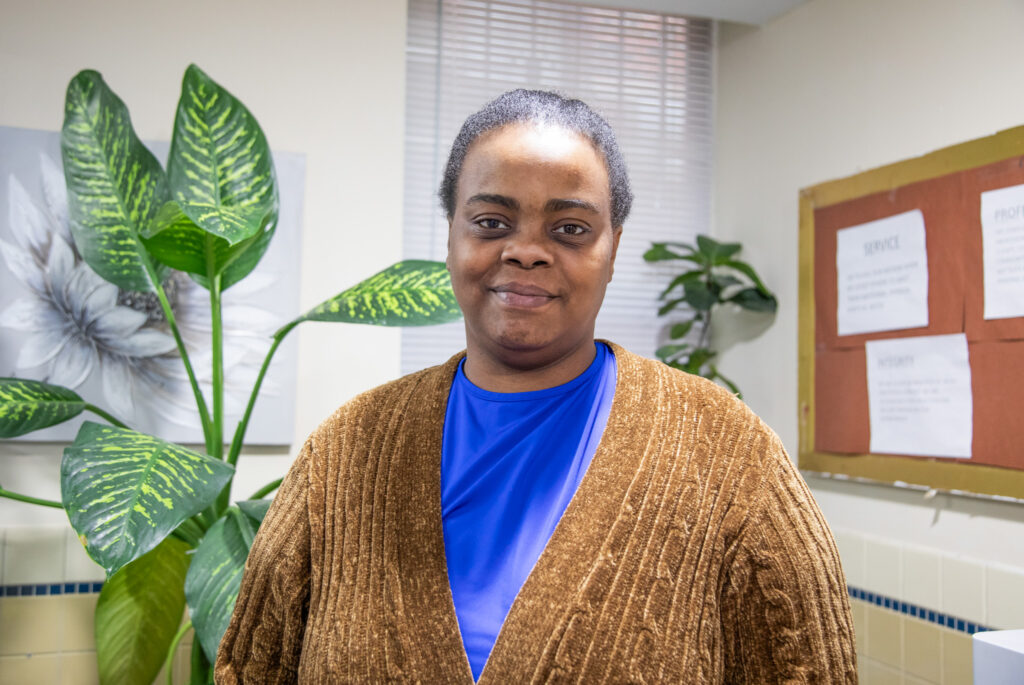 VOA-GNY client Shaniqua smiling in front of a leafy plant.