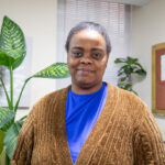 VOA-GNY client Shaniqua smiling in front of a leafy plant.