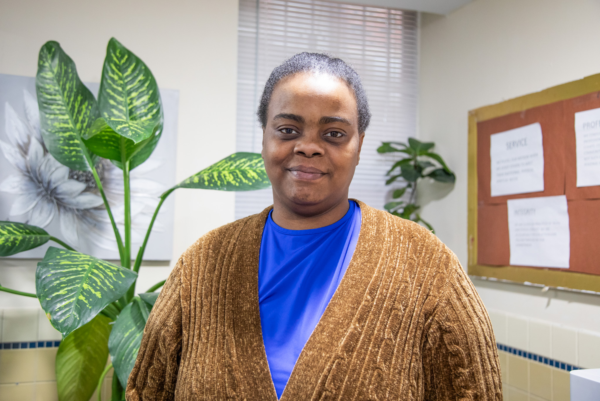 VOA-GNY client Shaniqua smiling in front of a leafy plant.