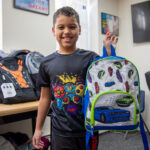 Smiling boy holding up a backpack.