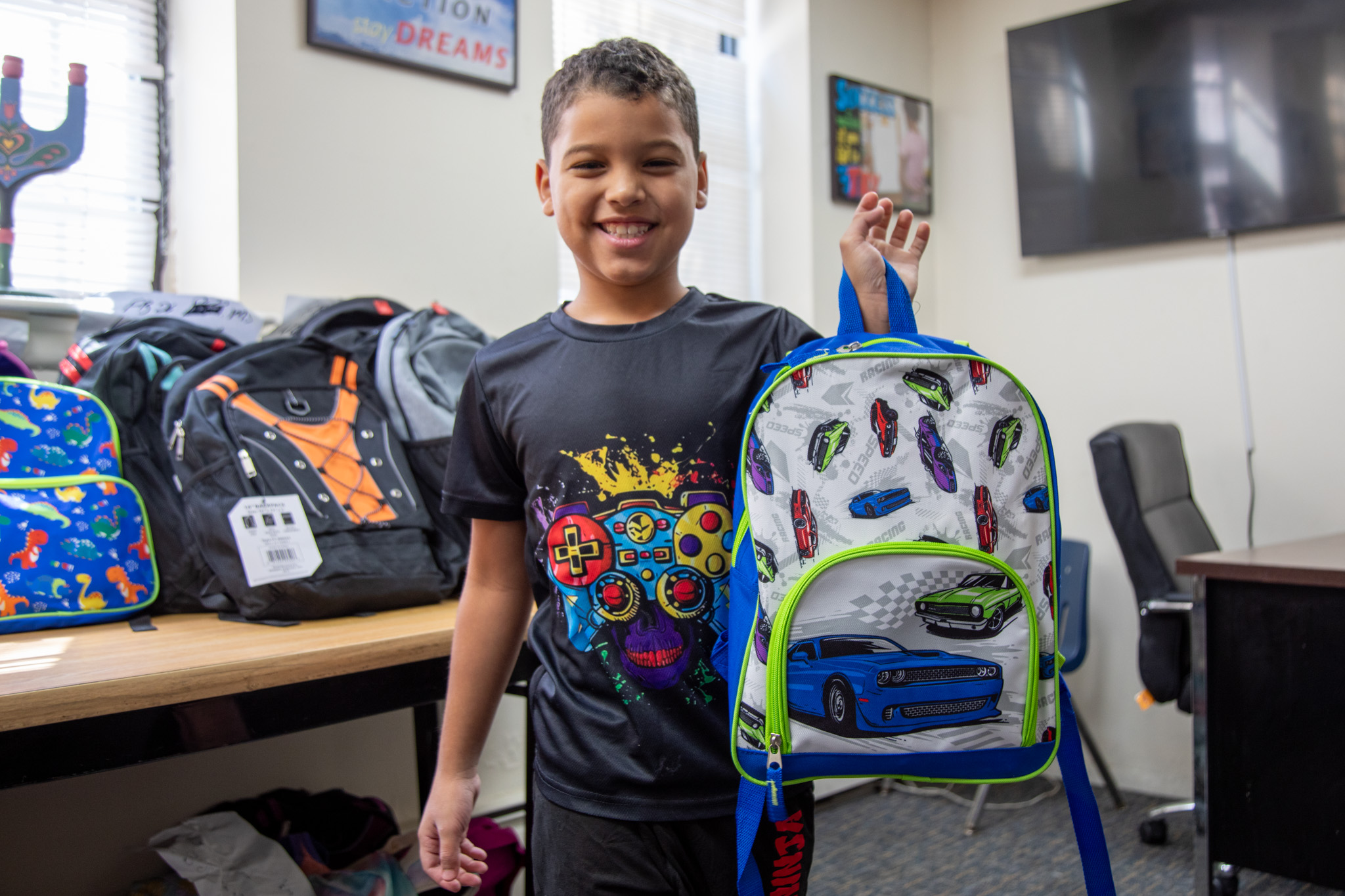 Smiling boy holding up a backpack.