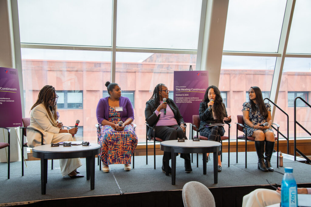 Panelists on stage with microphones with purple signs behind them. 